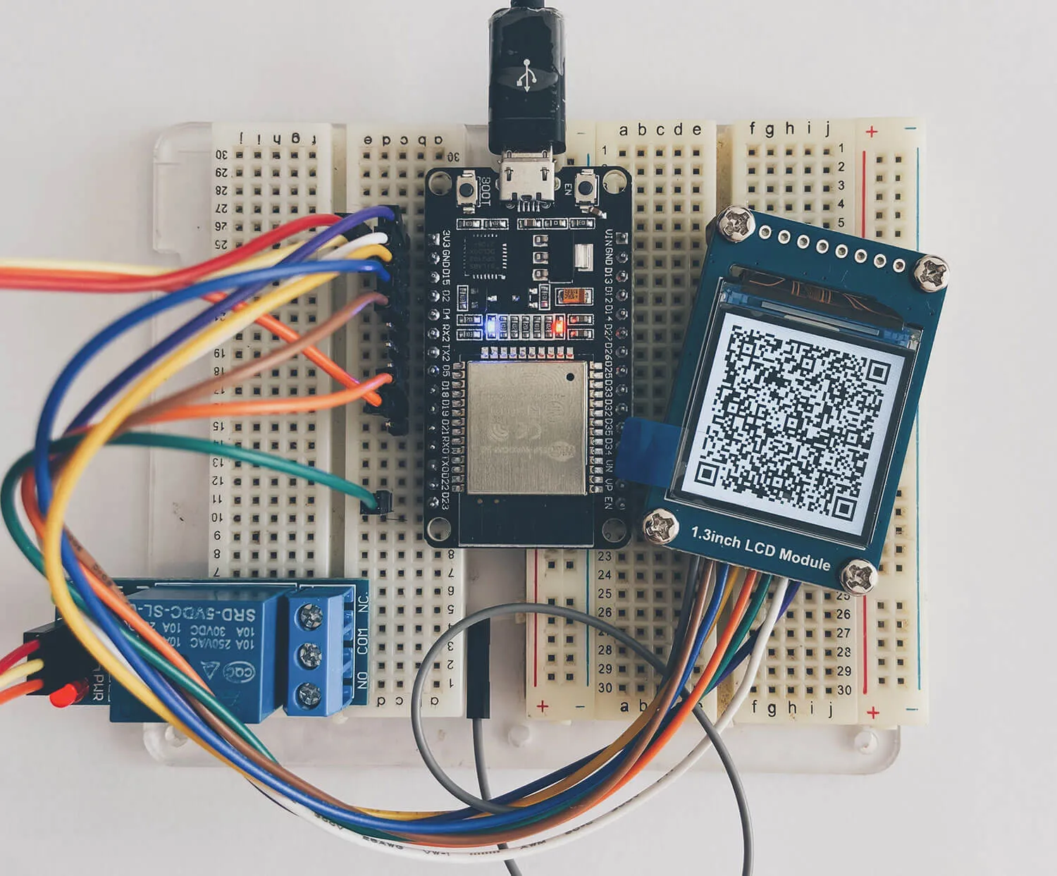 Prototipo en protoboard con un ESP32, un relé y una pantalla mostrando un QR