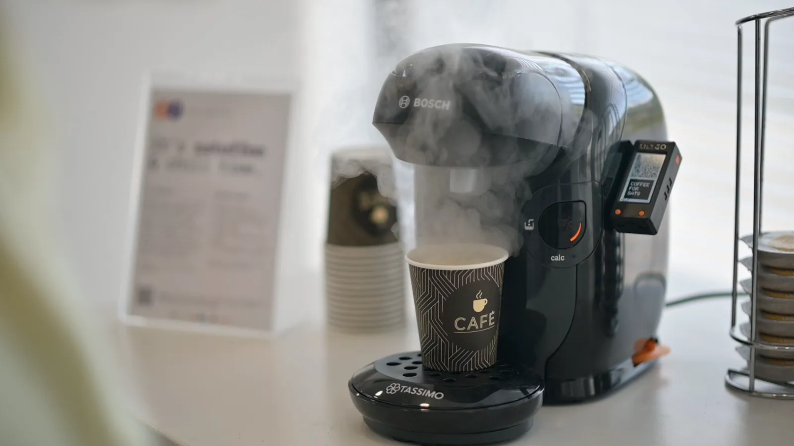 Un café recién hecho humeando junto a la pantalla de Satoffee